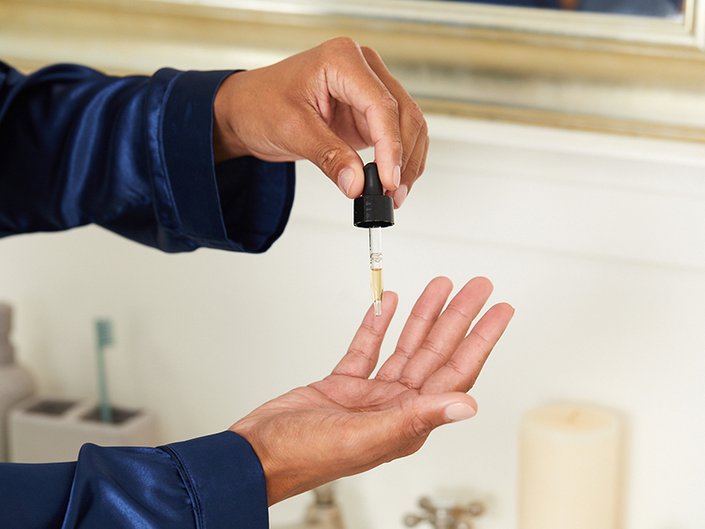 Picture of one hand with a dropper squeezing product onto another hand directly below